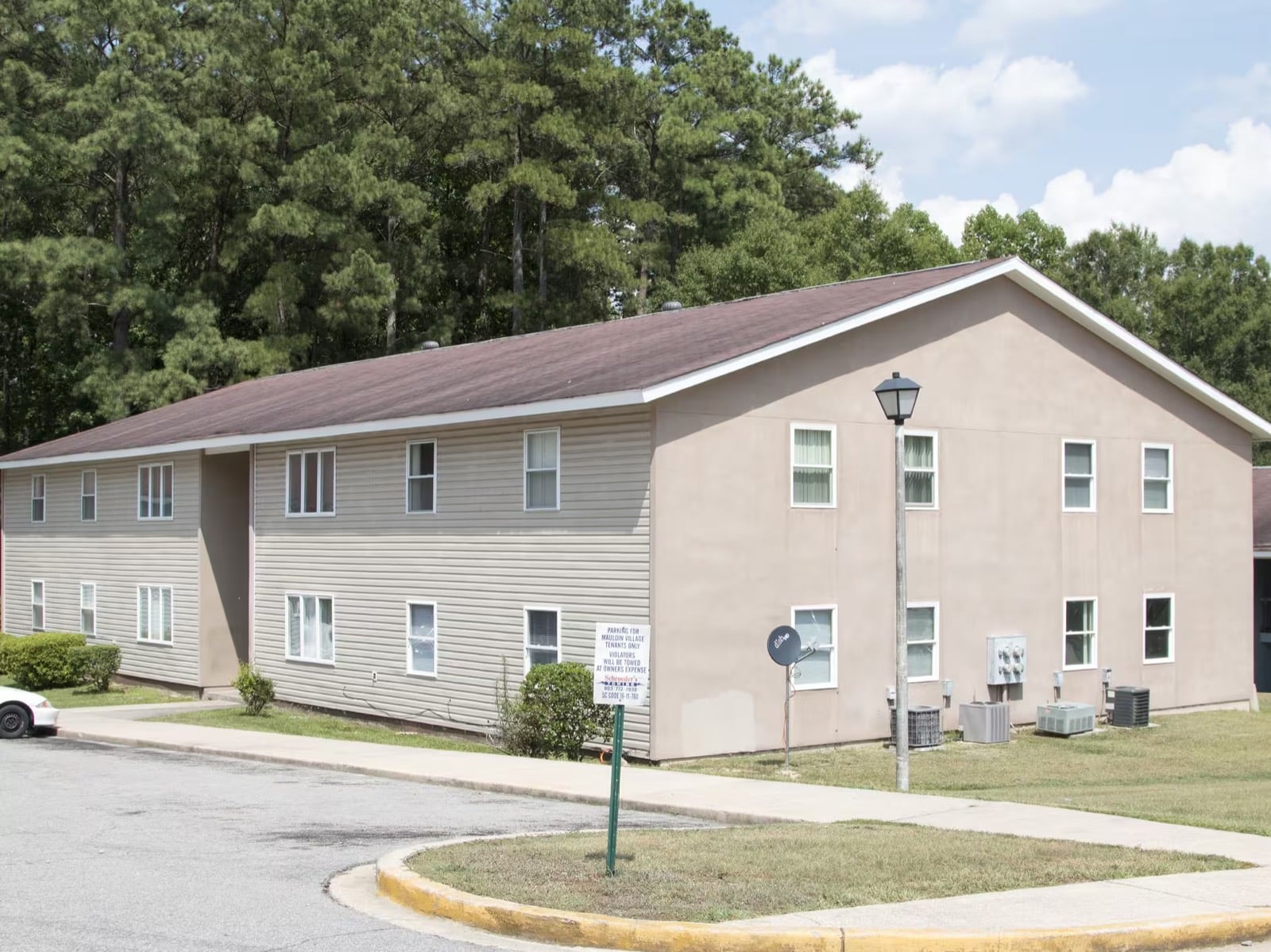 Two-story apartment building at Mauldin Village with lawn, lamppost, and pine trees behind