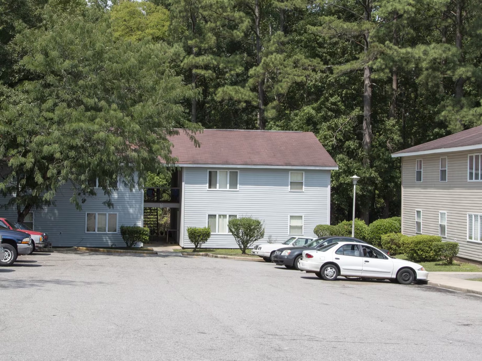 Two apartment buildings at Mauldin Village surrounded by tall pine trees, with resident parking in front